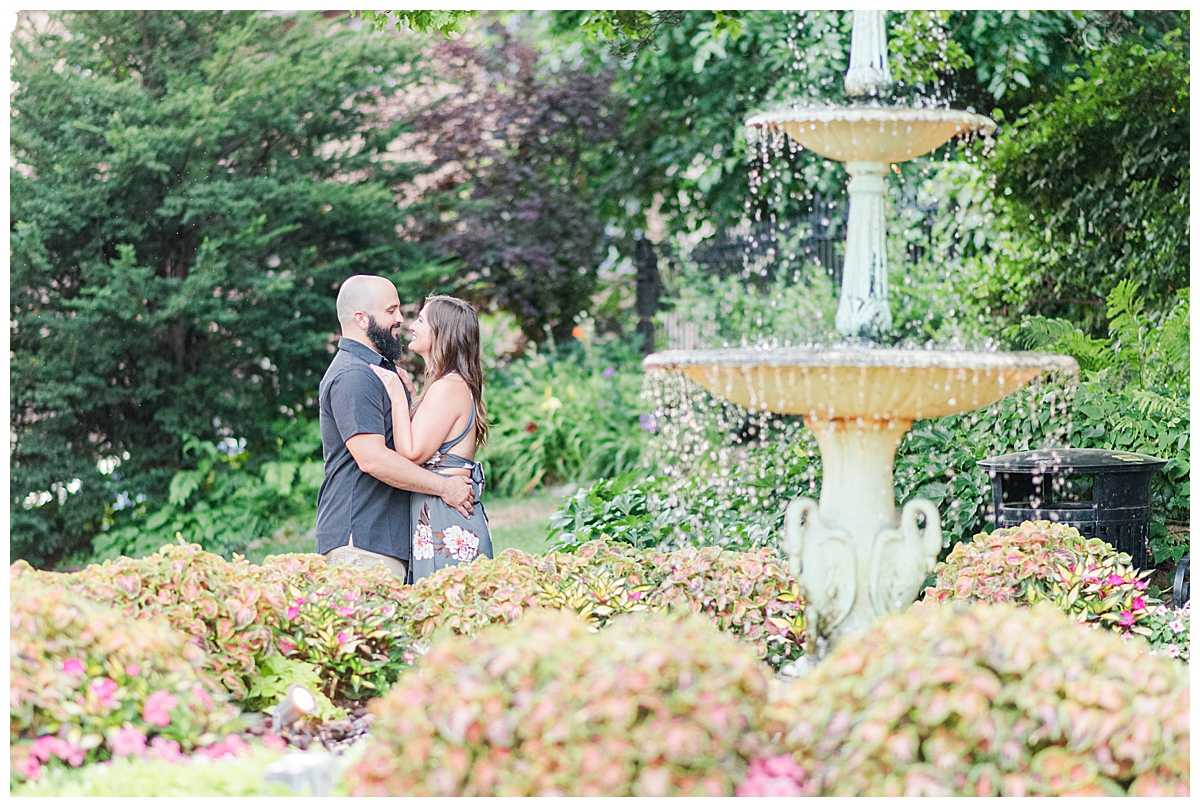 A couple kissing behind a fountain at Period Garden Park in downtown Madison for engagement photos