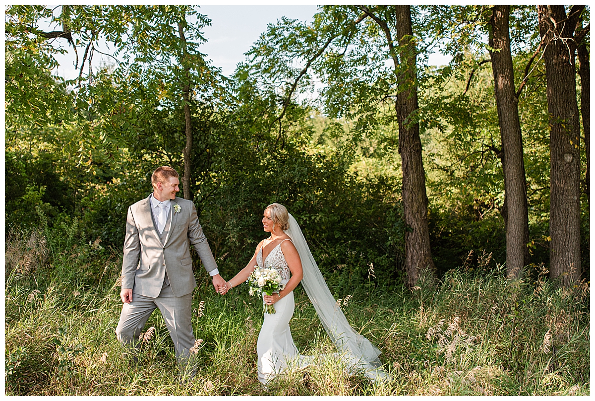 Bride and groom walking through a field with tall grass outside of The Eloise, a modern barn venue near Madison, Wisconsin