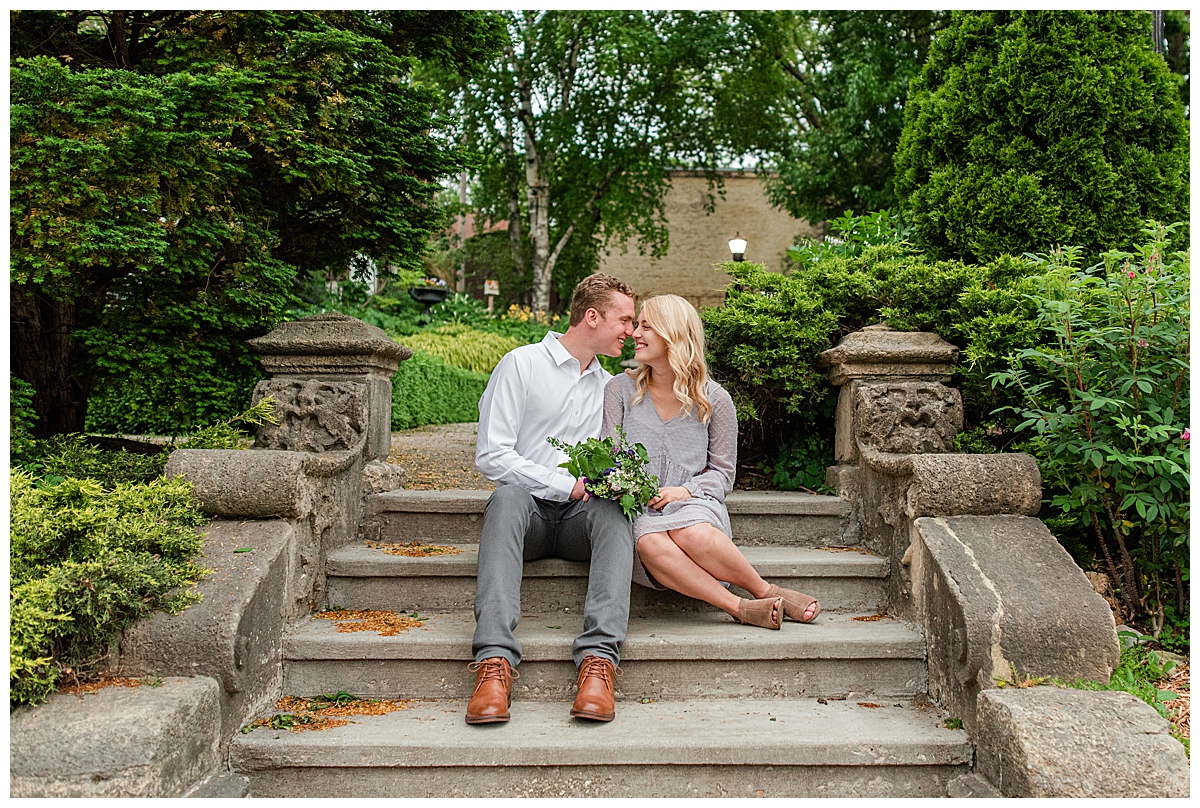 couple sitting together on the steps of period garden park for their madison engagement photos