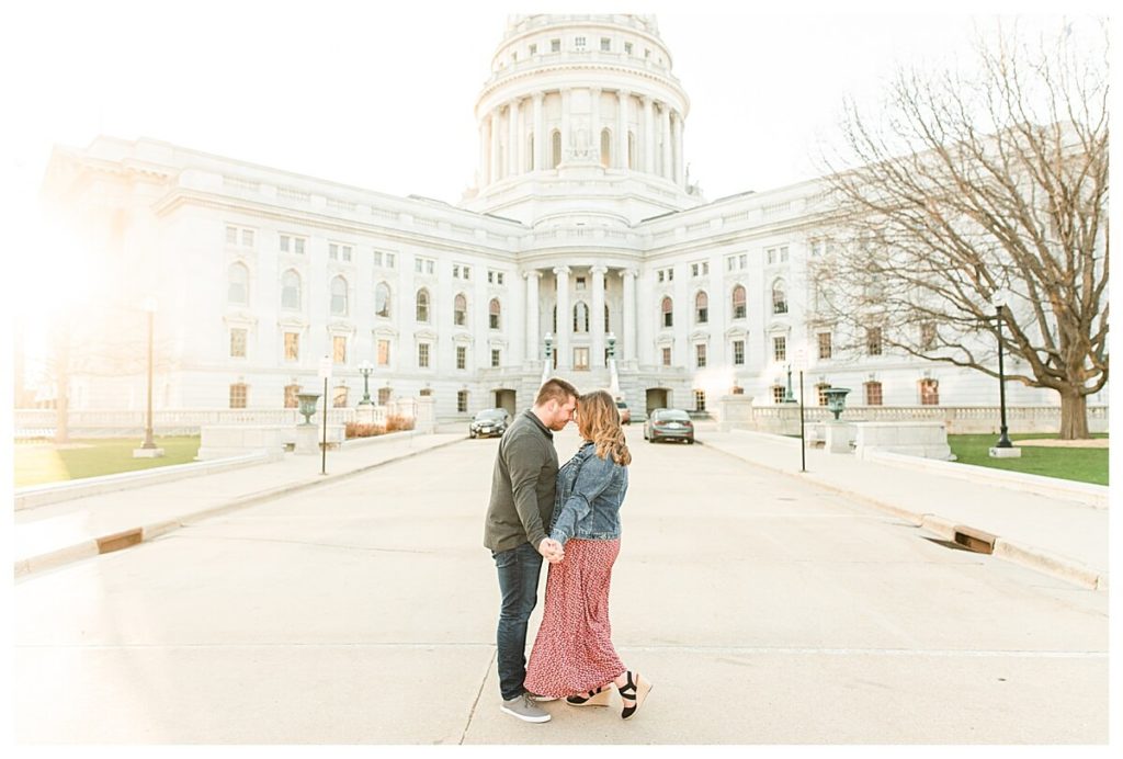 a couple poses for engagement photos on the capitol square in downtown madison