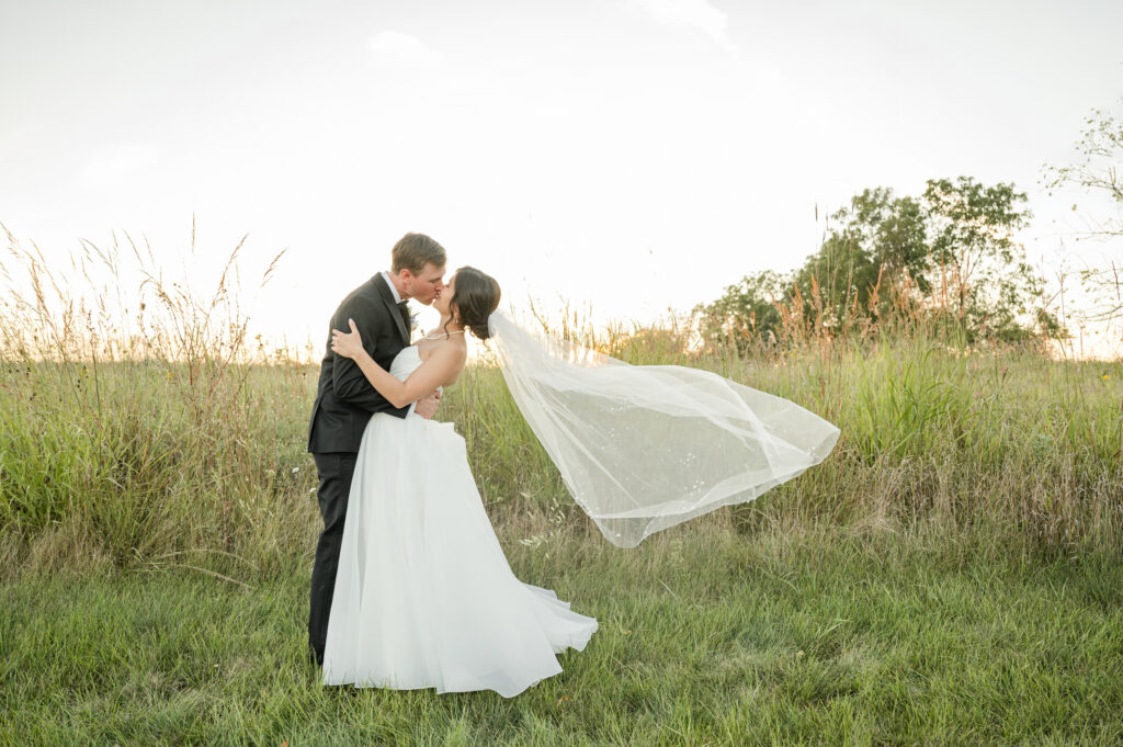 A bride and groom kissing with veil flying in the background, in front of the sunset